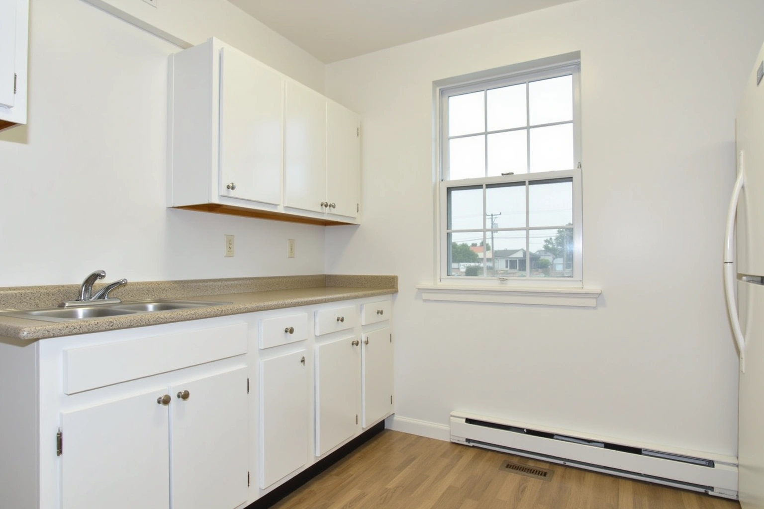 Plain white flat-panel cabinets with a speckled laminate counter and stainless double sink in a bare kitchen.