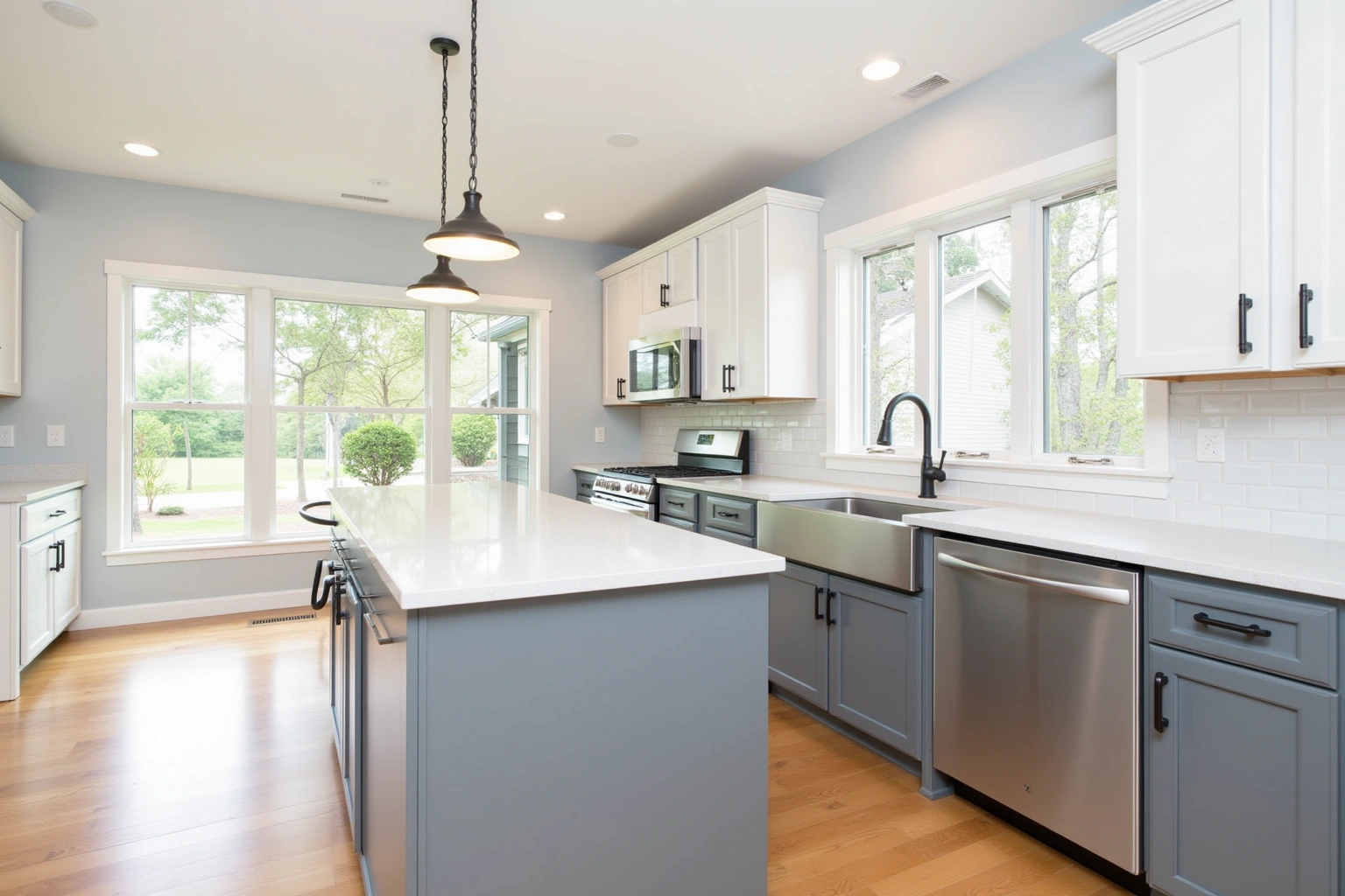 White shaker uppers over grey-blue base cabinets and island, matte black pulls, subway tile and a farmhouse sink.
