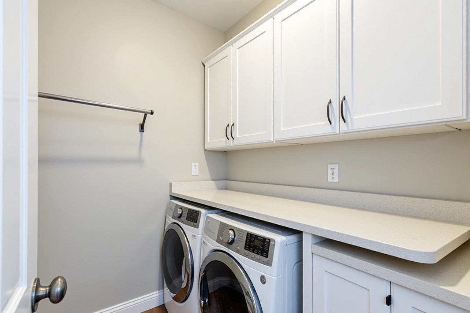 White shaker laundry cabinets and a quartz folding counter over a front-load washer and dryer, with a hanging rod.